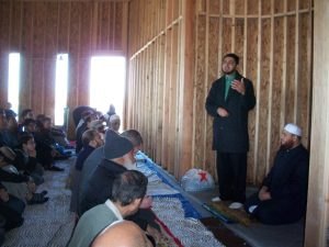 Men seated on the floor listening to a talk inside the framed prayer hall